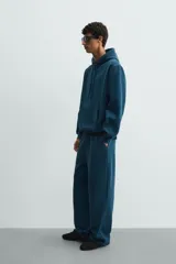 Pantalón jogger de corte relajado y pernera ancha, confeccionado en tejido de algodón con interior perchado. Presenta cintura elástica con cordón interior, bolsillos laterales y un bolsillo trasero de plastrón.