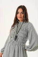 Vestido largo de rayas verticales en tonos gris y blanco, con cuello alto fruncido, mangas largas tipo globo con puños elásticos y cuerpo con diseño de nido de abeja hasta la cintura. Presenta una falda amplia con caída fluida.