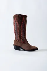 Bota texana de cuero negro con apliques de cuero marrón en los laterales y pespuntes en color crema. De caña media/alta y taco bajo. Diseño calado con motivos geométricos.