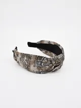 Vincha de pelo con nudo central, confeccionada en tela con estampado paisley en tonos beige y negro, con forro interior negro.