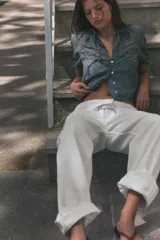 Camisa de cuello redondo con lazada frontal, manga corta abullonada con lazos ajustables y cierre frontal con botones. Presenta detalles de bordados y encaje a tono sobre una base de tela tipo chambray.