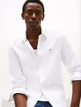 Camisa blanca de algodón con tecnología Flex, corte slim fit, cuello abotonado, mangas largas con puños redondeados y logo de Tommy Hilfiger bordado en el pecho.