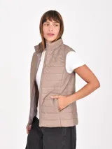 Chaleco acolchado de diseño matelasse, color beige, con cuello alto, cierre frontal y bolsillos laterales.