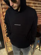 Canguro de algodón color negro con corte oversize, capucha y bolsillo frontal tipo canguro. Presenta un pequeño bordado con el logo de la marca en el centro del pecho.