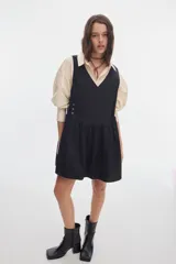 Vestido corto negro de algodón, con escote en V cruzado, sin mangas y falda con fruncido en la cintura.