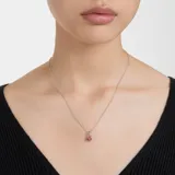 Colgante con cadena de eslabones plateados y un dije principal con una piedra roja de talla cuadrada rodeada de cristales rojos más pequeños. El engarce del dije es plateado.