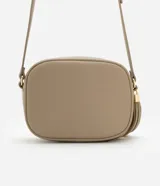 Cartera bandolera pequeña color beige, confeccionada en poliuretano con textura granulada. Presenta cierre superior con cremallera, correa larga ajustable y detalle de borla decorativa en el lateral con herrajes dorados.