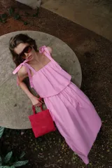 Vestido midi de color rosado con escote recto elástico y tirantes anchos con lazos ajustables. Presenta cintura elástica y bolsillos laterales ocultos en la costura.