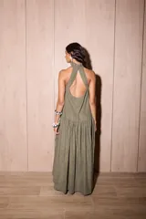 Vestido largo holgado color verde oliva, con escote halter y cuello alto con volado. Presenta un corte con fruncido a la altura de la cadera que genera un maxi volado en la falda.