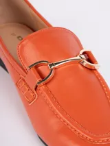 Mocasines color naranja de símil cuero con aplique metálico dorado en la parte superior, plantilla acolchada y taco de 1,5cm.