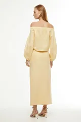 Blusa color amarillo claro, con escote off-shoulder, mangas largas abullonadas y dos bolsillos con solapa en el pecho.
