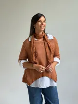 Sweater de punto color naranja con diseño asimétrico, que incluye una bufanda a juego con detalles bordados y una camisa blanca de base integrada.