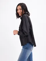 Camisa negra de manga larga con detalles de alforzas (tablas) en el frente, cuello camisero y cierre frontal de botones.