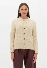 Cardigan de punto trenzado color beige, con cuello redondo, cierre frontal con botones dorados y mangas largas con puños acanalados.