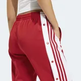 Pantalon deportivo Adidas modelo Adibreak, color rojo con franjas laterales blancas y botones a presión. Presenta cintura elástica y corte holgado.