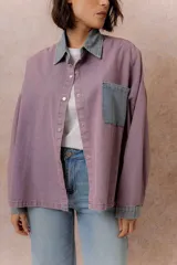 Camisa lila de calce relajado y manga larga, con cuello clásico, puños y bolsillo delantero en denim contrastante. Cierre frontal con broches metálicos.