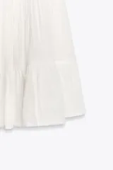 Vestido corto negro de gasa con escote recto y tirantes finos ajustables. El corpiño tiene fruncido elástico y el ruedo es escalonado con volados. Presenta un detalle de encaje a tono en el borde del escote.