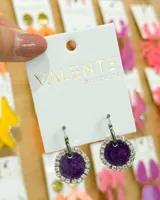 Aros colgantes con aro de acero plateado y dije circular con centro de tela color violeta y borde de strass plateado.
