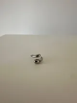 Anillo abierto de diseño minimalista con forma de gota en los extremos, fabricado en acero quirúrgico hipoalergénico de acabado plateado.