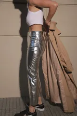 Pantalón de ecocuero metalizado color plateado, de corte capri semi oxford y tiro medio-alto. Presenta cierre frontal con botón metálico y costura horizontal a la altura de la rodilla.