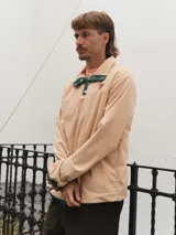 Buzo de pana color beige con cuello polo abotonado y bolsillo en el pecho.