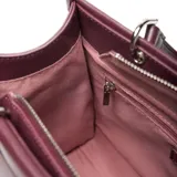 Cartera estructurada mediana de material símil cuero color bordó, con doble manija fija y correa larga regulable y desmontable. Presenta solapa frontal con botón imantado y cierre superior con cremallera metálica.