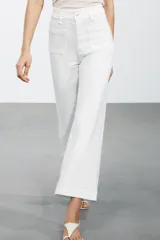 Pantalón de jean blanco de tiro alto y corte wide leg, con bolsillos delanteros y traseros. Cierre frontal con cremallera y botón metálico.