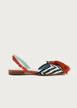 Sandalias planas destalonadas confeccionadas en rafia trenzada con patrón de zigzag en tonos azul marino y crudo. Tienen punta cerrada con una borla decorativa de flecos naranjas en el empeine, y una tira trasera ajustable de cuero naranja con hebilla metálica dorada.