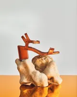Sandalia de cuero metalizado rosado con taco cuadrado medio y tira ajustable con hebilla en el tobillo.