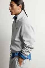 Sudadera gris de corte relaxed fit con cuello alto y cierre frontal de cremallera corta, confeccionada en algodón con interior de rizo afelpado. Presenta mangas largas, puños y bajo de rib, y un parche bordado con el logotipo de Fruit of the Loom en el pecho. Colección especial Fruit of the Loom x Zara.