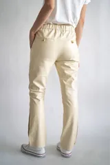 Pantalón de cuero color beige, con cintura elástica, bolsillos laterales y detalle de botones metálicos en los tobillos.