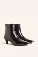 Bota de caña corta confeccionada en cuero vacuno color chocolate con acabado brillante. Presenta punta fina, cierre posterior y taco chupete bajo.
