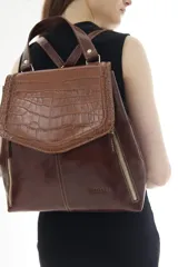 Mochila de cuero vacuno marrón con acabado pulido, solapa en forma de V y costuras decorativas. Cuenta con cremalleras laterales y asas ajustables.