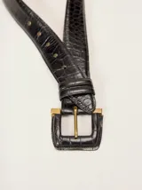 Cinturón de cuero negro con textura estilo croco, hebilla forrada en cuero con detalles metálicos dorados.