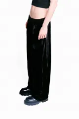 Pantalón de terciopelo negro de corte medio, con cintura elástica, dos bolsillos laterales, logo de la marca bordado en el frente y detalles de costuras delanteras. Es una prenda unisex.