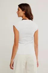 Remera blanca de punto acanalado, de calce entallado y largo a la cadera, con escote redondo, mangas cortas tipo casquillo y costuras en relieve.