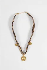 Collar con tira de tela estampada en animal print, adornado con un dije central grande en forma de sol y pequeños dijes de sol distribuidos a lo largo de la tira, todos en tono dorado.