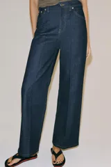 Jeans wide leg de tiro alto en color azul oscuro, con trabillas en la cintura, diseño de cinco bolsillos, nervios delanteros marcados y pespuntes a contraste. Cuenta con cierre frontal de cremallera y botón metálico.