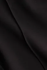 Pantalón de punto elástico en color negro, de corte ajustado con pliegue cosido frontal y cierre en los bajos.
