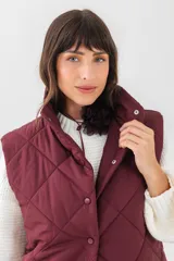 Chaleco acolchado negro con diseño de rombos, cuello alto y cierre frontal con botones a presión. Cuenta con bolsillos laterales.
