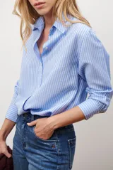 Camisa de mujer a rayas verticales blancas y rosadas, con cuello clásico, cierre de botones frontal y mangas largas con puños abotonados.