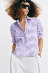 Camisa de cuello solapa y mangas cortas abullonadas, con diseño de rayas verticales en tonos rosados y celestes, decorada con lentejuelas bordadas.