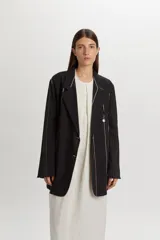 Chaqueta negra de corte oversize y diseño desestructurado, con solapas clásicas, cierre frontal de dos botones y sutil estampado de rayas verticales finas.