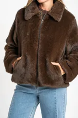 Abrigo de piel sintética en color marrón, con cuello clásico, cierre frontal con cremallera y mangas largas.