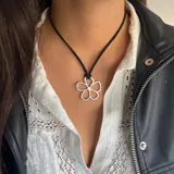 Gargantilla con cordón negro y dije plateado con forma de flor de cinco pétalos.
