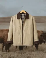 Campera de estilo workwear en color beige, confeccionada en tela resistente con cuello y puños de pana en color marrón chocolate. Presenta cierre frontal, dos bolsillos frontales tipo parche y forro interior de tela escocesa.