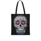 Tote bag de color negro con estampado frontal de una calavera estilo calaca mexicana en tonos violetas, con ojos en forma de corazón y detalles gráficos coloridos.