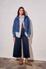 Campera bomber de jean con corte oversize, cierre frontal y cuello alto con botones a presión. Presenta mangas amplias y puños ajustados.