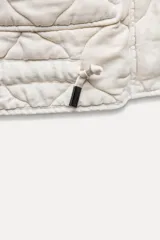 Chaleco gris acolchado con cuello alto, cierre frontal con cremallera metálica, bolsillos de plastrón en delantero y bajo ajustable con cordones.