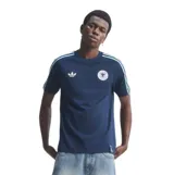 Remera de estilo urbano Adidas inspirada en la selección de fútbol de Alemania. Es de color azul marino con las icónicas tres tiras en celeste sobre los hombros y mangas. Presenta el logo del trébol de Adidas en blanco en el pecho derecho y el escudo de la federación alemana en el izquierdo.